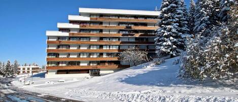 A multi-story hotel with a modern design, featuring balconies and a snow-covered landscape.