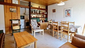 A cozy living room with a wooden table, chairs, and a sofa. There is a kitchen area with cabinets and a refrigerator. - 300m from resort center, 2nd floor, balcony, tv, 55m², Chamrousse (Chamrousse)