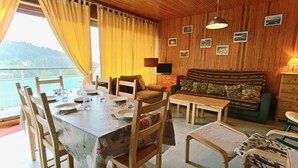 A dining area with a table set for four, wooden chairs, a sofa, and a television. - 300m from resort center, 2nd floor, balcony, tv, 55m², Chamrousse (Chamrousse)