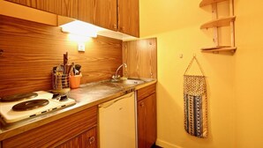 Une cuisine de taille réduite, avec des meubles de rangement en bois, un évier, une cuisinière et un petit réfrigérateur.