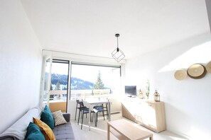 Un soggiorno luminoso e moderno con divano, poltrone, un tavolo da pranzo e un'ampia finestra con vista sulle montagne.