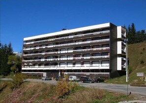 Un edificio a più piani con balconi, situato vicino a una strada con auto parcheggiate.