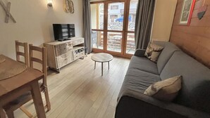 A living room with a sofa, a TV, a wooden dining table, and a small round table.