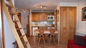 Cocina compacta con armarios de madera, salpicadero de azulejos y microondas integrado. Una escalera de madera está apoyada en la pared, y un sofá rojo se encuentra en primer plano.