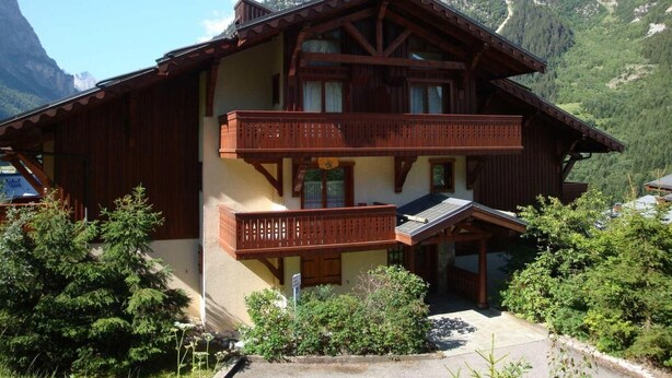 Una cabaña de madera de dos pisos con balcones, ubicada frente a un paisaje montañoso.