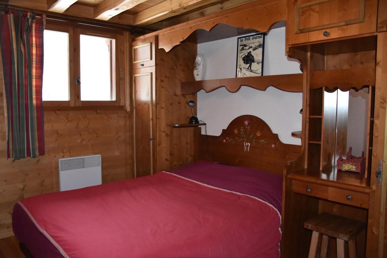 Une pièce en bois avec un lit, une commode, un miroir et une fenêtre avec des rideaux.