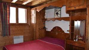 Una habitación de madera con una cama, un tocador, un espejo y una ventana con cortinas.