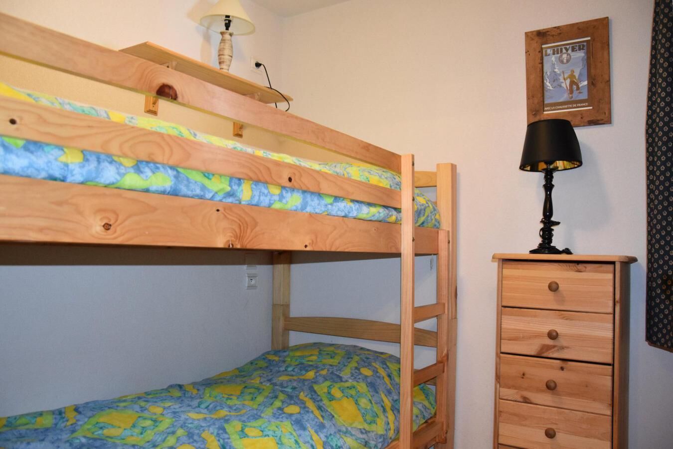 Ein Etagenbett mit Lampe, eine Kommode mit Schubladen und ein gerahmtes Bild an der Wand.