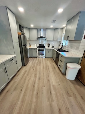 A modern kitchen with grey cabinets, stainless steel appliances, and a wooden floor. - Modern Chic 4-Bedroom Home with Wood Stove Fireplace (Flagstaff)