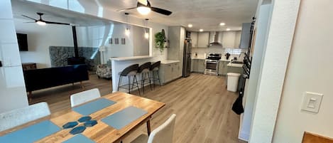 A modern kitchen with a central island, bar stools, and a dining area with a wooden table and chairs.