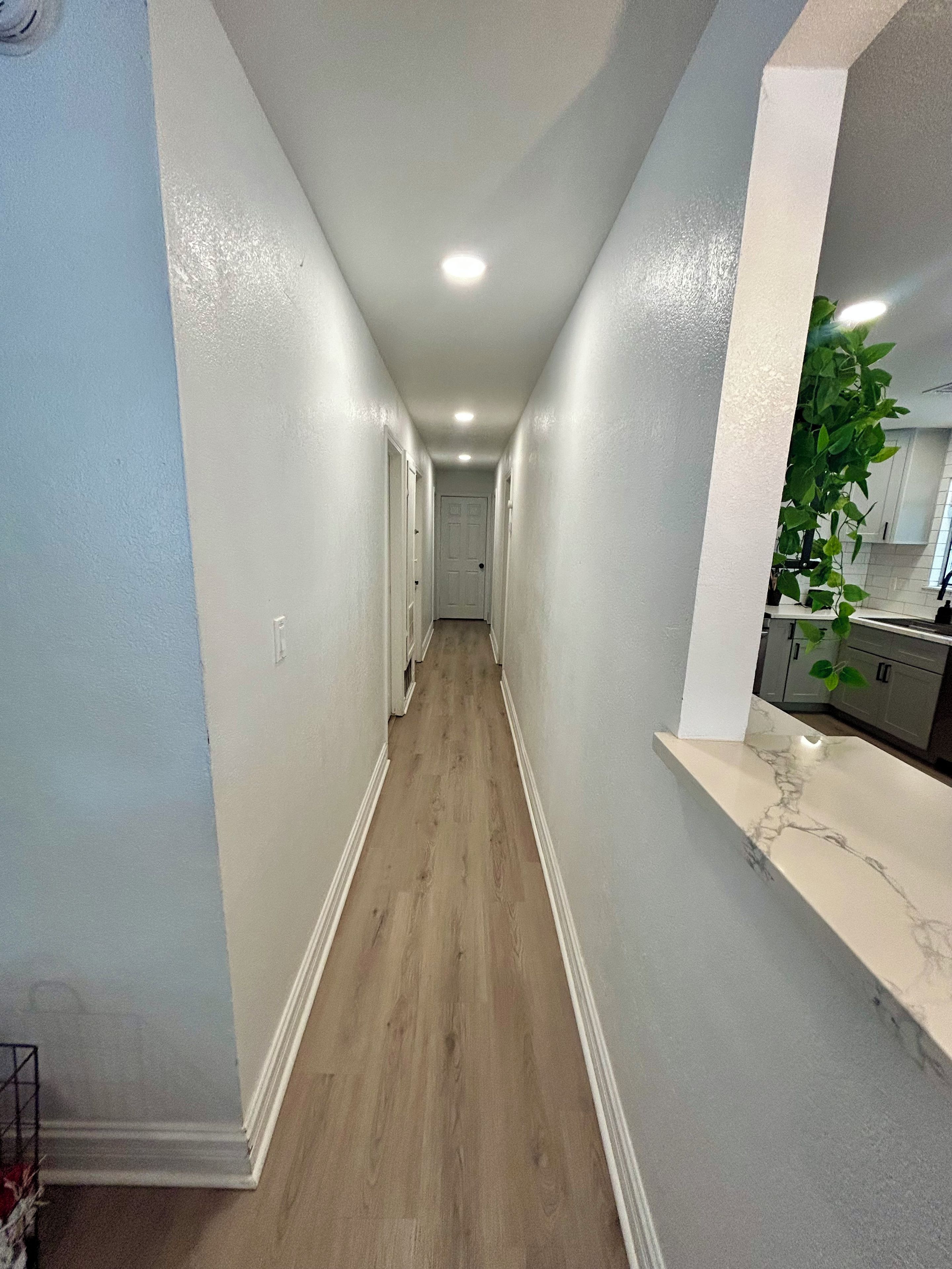 A narrow hallway with a wooden floor, white walls, and a white door at the end.
