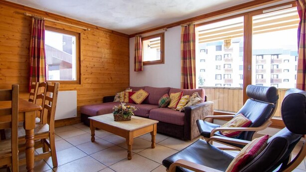 Un salon chaleureux avec des murs en bois, un canapé, une table basse et un balcon offrant une vue sur les immebles.