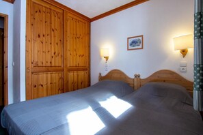 A bedroom with two beds, wooden headboards, and wall-mounted lamps.