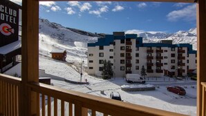 Un paysage de montagne enneigé, avec un bâtiment doté de nombreux balcons et un télésiège en arrière-plan.