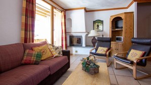Un salon comprenant un canapé, deux fauteuils, une cheminée, un téléviseur et un meuble en bois.