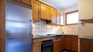Une cuisine avec des meubles de rangement en bois, un réfrigérateur en acier inoxydable, un évier et une fenêtre.