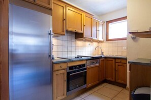 A kitchen with wooden cabinets, a stainless steel refrigerator, a sink, and a window.