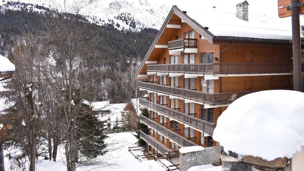 Un edificio de madera de varios pisos con balcones, rodeado de árboles y montañas cubiertas de nieve.