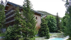 Un edificio de varios pisos con balcones, rodeado de árboles frondosos y una piscina.