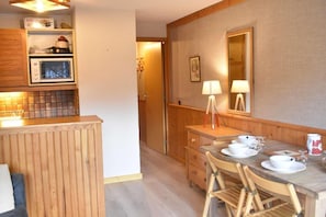 Une cuisine compacte équipée d’un four à micro-ondes, d’un meuble en bois et d’un coin repas avec une table dressée pour deux personnes.