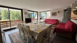 Un comedor con una mesa dispuesta para seis personas, rodeada de sillas. Se observa un sofá rojo y un aparador verde al fondo.