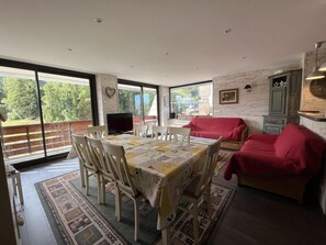 Un comedor con una mesa dispuesta para seis personas, rodeada de sillas. Se observa un sofá rojo y un aparador verde al fondo.