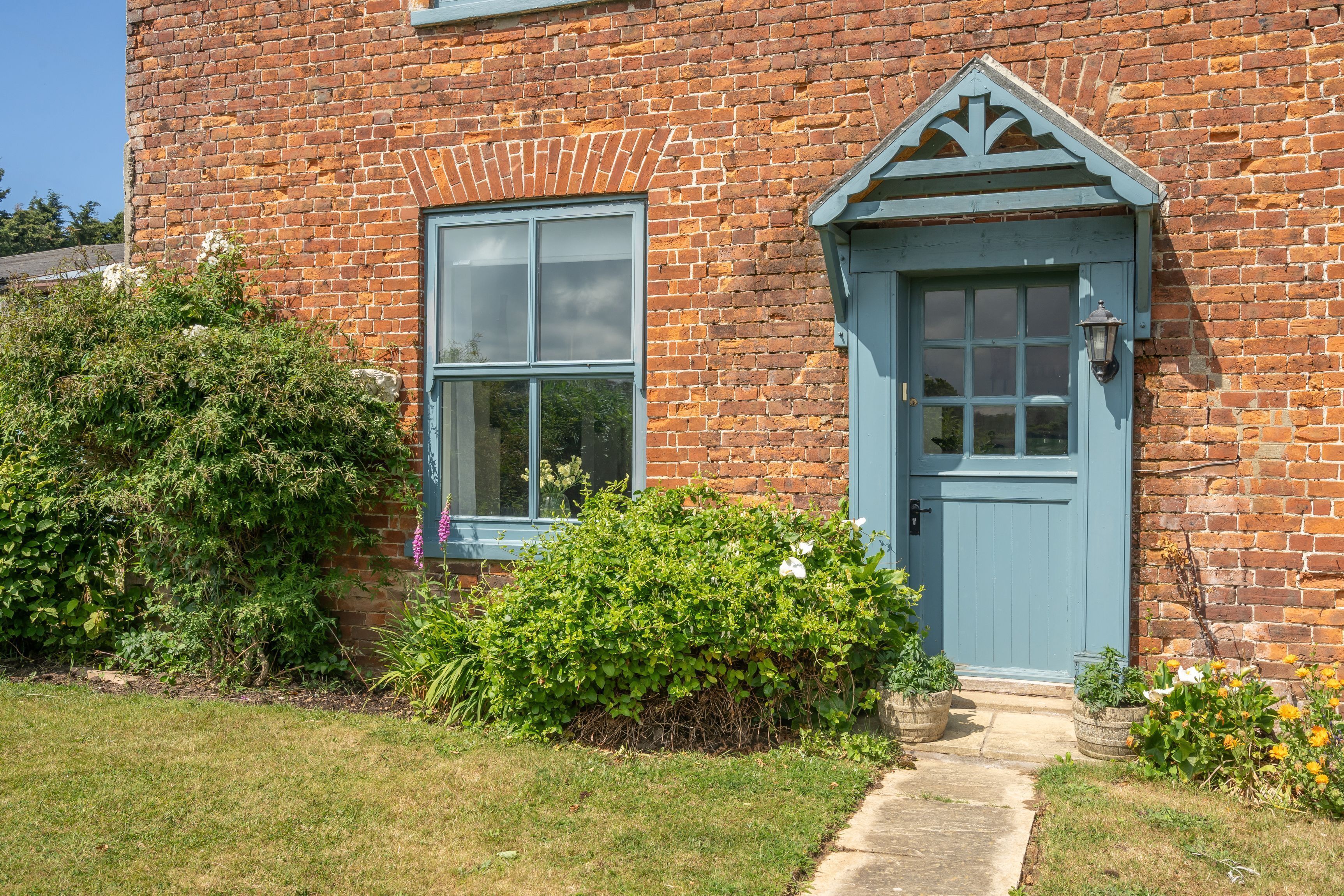 A brick house with a blue door and window, surrounded by greenery.