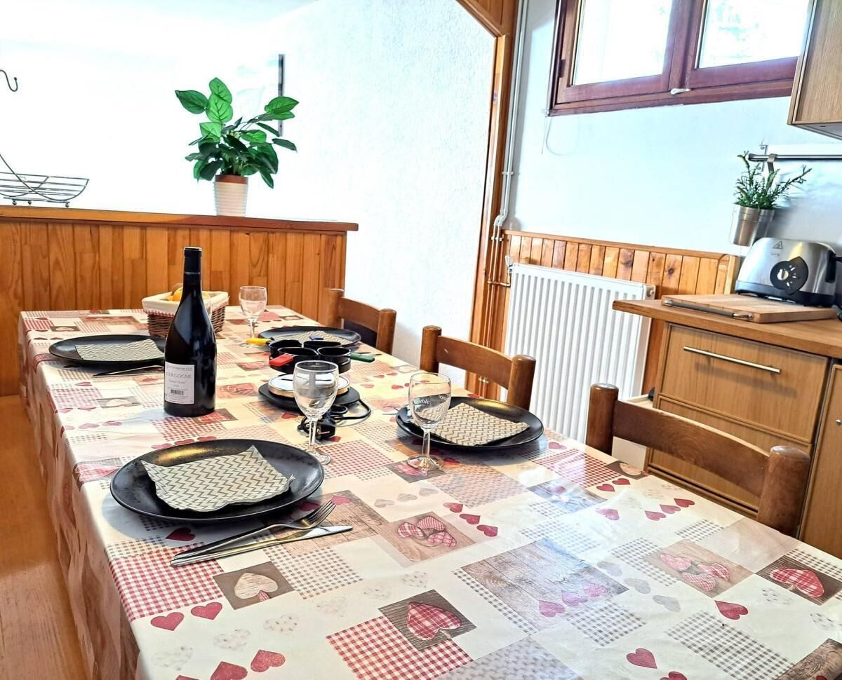 A dining table set with plates, glasses, and a bottle of wine, surrounded by wooden chairs and a radiator.