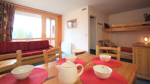 A cozy room with a wooden table set for tea, a red sofa, and a bunk bed. - 50m from resort center, 2nd floor, view valley, balcony, tv, 40m², Les Arcs (Les Arcs)