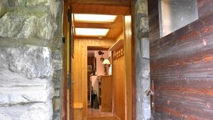 Un pasillo interior de madera con una pared de piedra a un lado y una puerta de madera al otro.