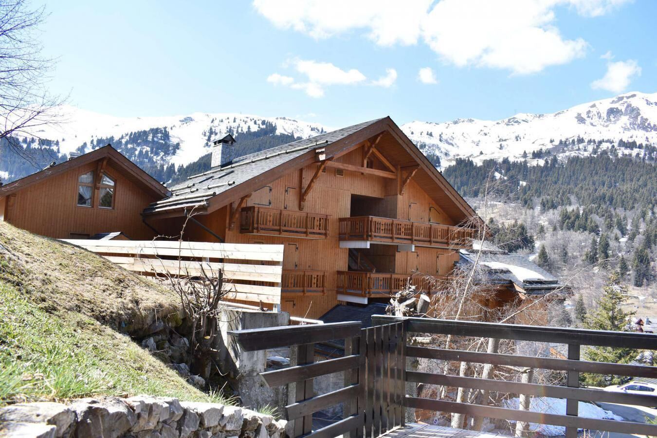 Een houten chalet met balkon, gelegen tegen een bergachtige achtergrond.
