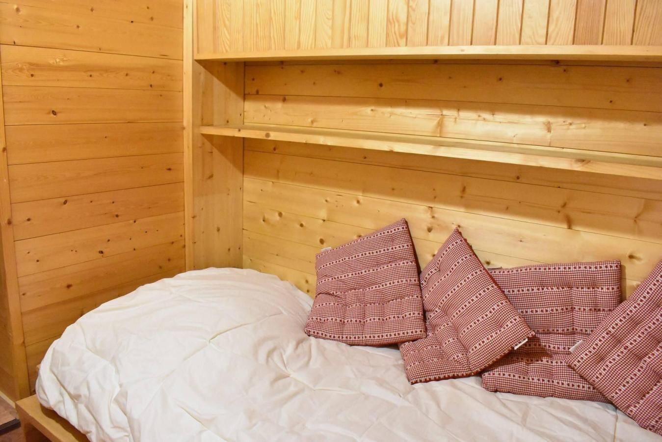 En stuga med träpanel, ett rum med en säng, kuddar och en hylla ovanför sängen.