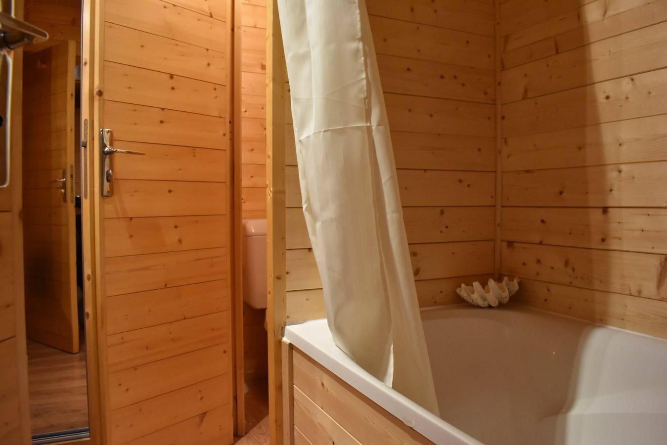 A wooden cabin bathroom with a bathtub, wooden walls, and a shower curtain.