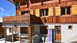 A wooden chalet with a stone facade, a balcony, and a ski lift visible in the background.
