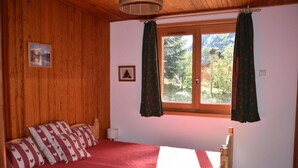 A bedroom with wooden walls, a bed with heart-patterned pillows, a window with curtains, and a picture on the wall.