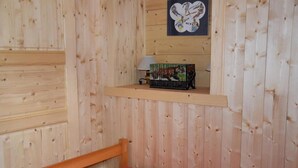 A wooden room with a bed, a shelf with a picture, and a small table with a lamp.