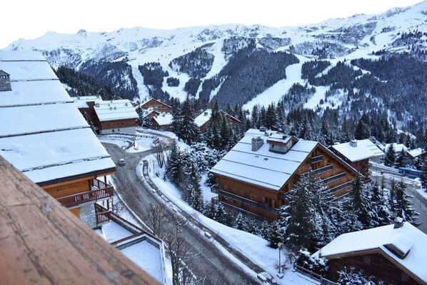 A snow-covered mountain village with wooden buildings, a winding road, and a view of the surrounding mountains.