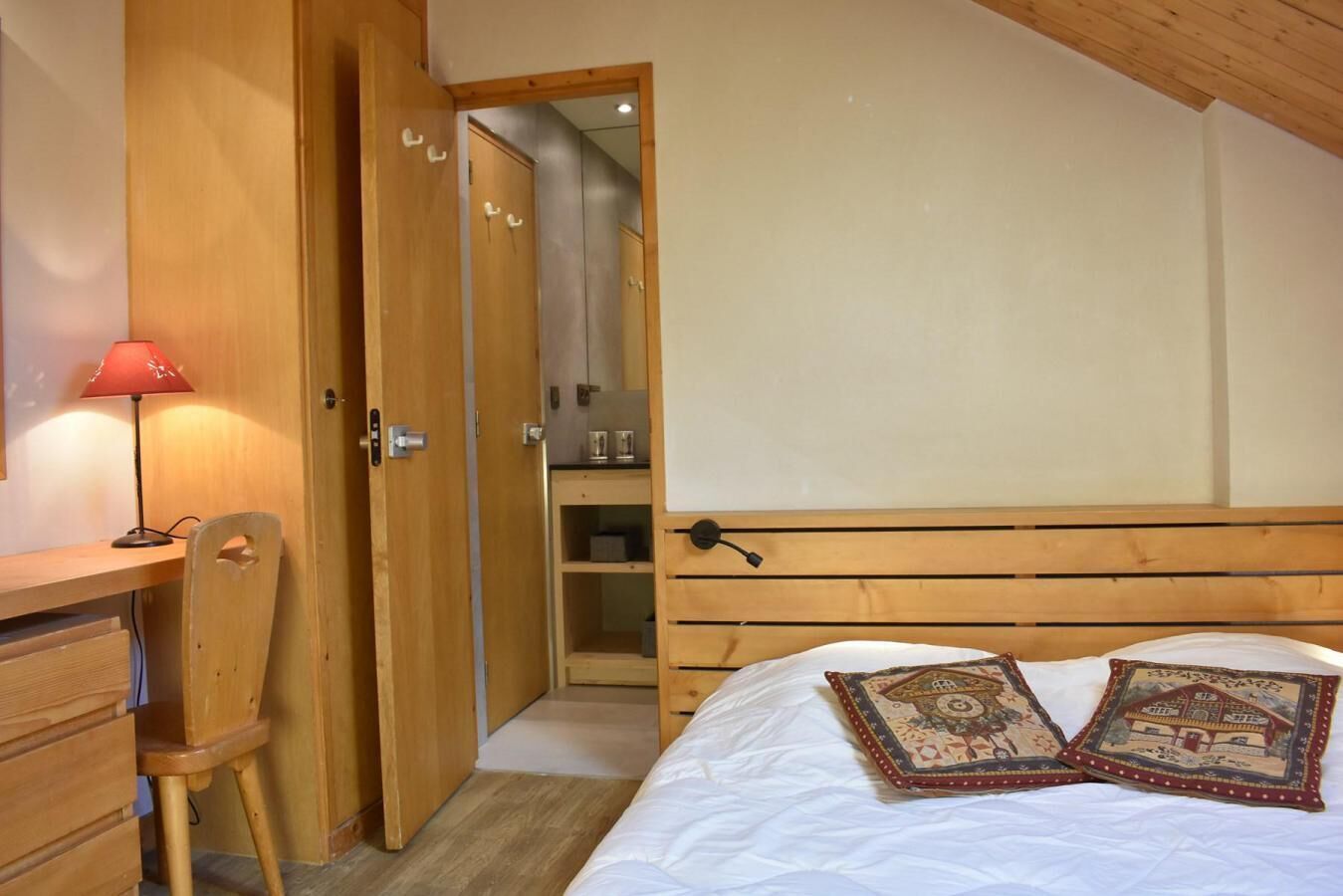 Une chambre à coucher avec une tête de lit en bois, un bureau avec une chaise, une lampe rouge et un lit agrémenté d’oreillers décoratifs.