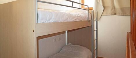 A bunk bed with a ladder, a window with curtains, and a wooden floor.