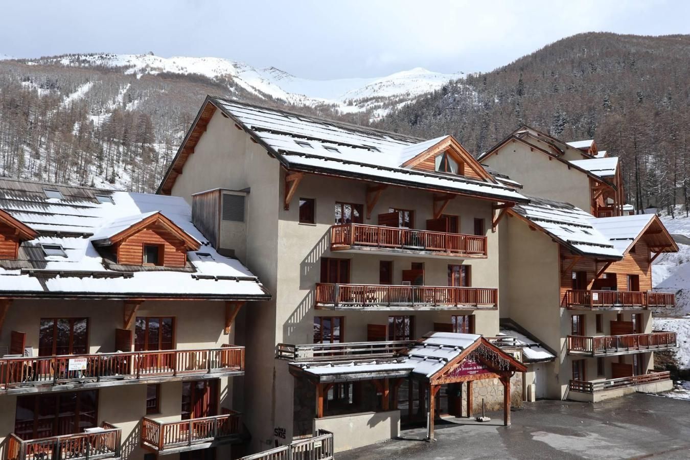 A multi-story hotel with balconies, ski slopes in the background, and a snowy landscape.