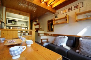 Um quarto aconchegante com uma mesa de jantar de madeira, um sofá e uma área de cozinha com micro-ondas e prateleiras.