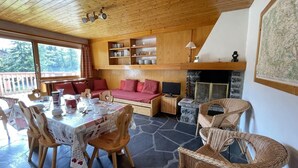 A cozy room with a dining table set for four, a sofa, wicker chairs, a fireplace, and wooden shelves with dishes.