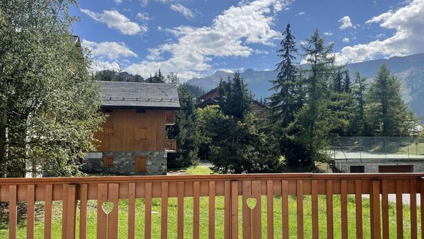A wooden cabin with a stone base, surrounded by trees and mountains in the background.