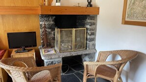 A cozy room with a stone fireplace, wicker chairs, a television, and a wooden shelf with decorative items.