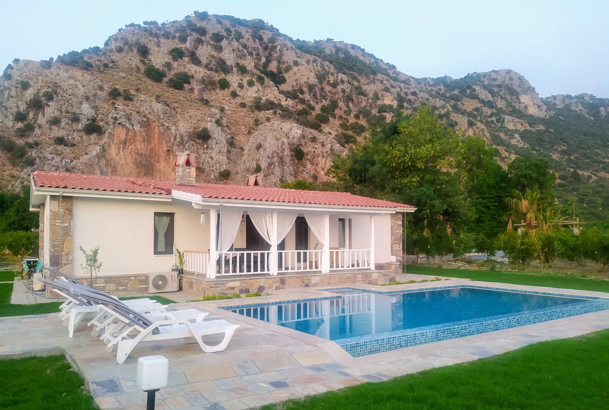 A house with a swimming pool, a stone chimney, and a view of a mountainous landscape.