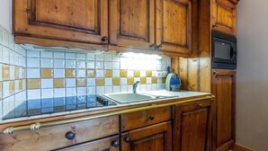 Una cocina con armarios de madera, un salpicadero de azulejos, un lavamanos de acero inoxidable y un microondas.