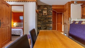 Una mesa de madera con sillas, una pared de piedra y una cama frente a una pared roja.