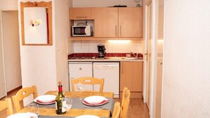 Comedor con una mesa preparada para cuatro, una botella de vino y copas. Hay un microondas y una cafetera en la encimera.