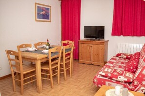 Una sala de estar acogedora con una mesa de comedor de madera, cortinas rojas, un televisor y un sofá estampado.