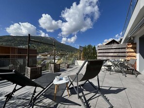 A rooftop terrace with outdoor furniture, a table with items, and a view of a mountain.